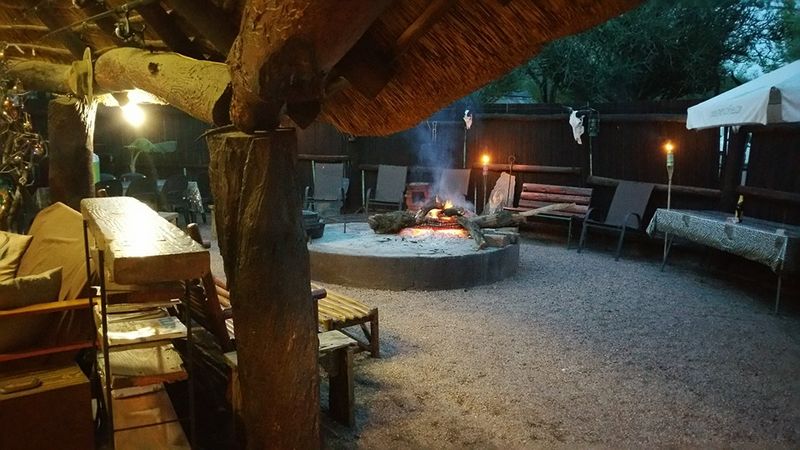 A fire burning in the open boma at dusk under thatch, with benches, paraffin torches and a gravel floor