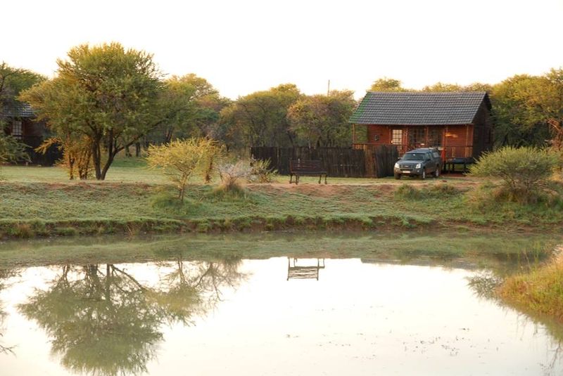A Zebra Log Cabin standing on the bank of one of the farm dams at first light, reflected in still water